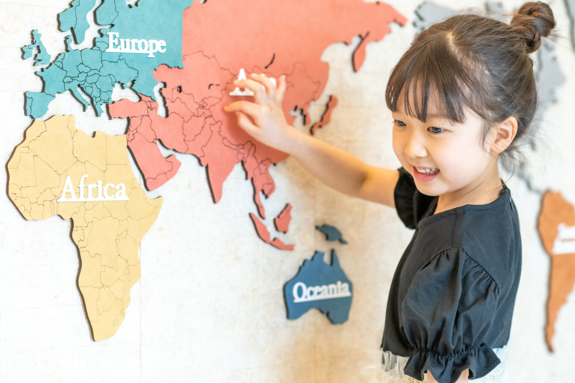 カラフルで立体的な世界地図を指さす女の子の写真です。