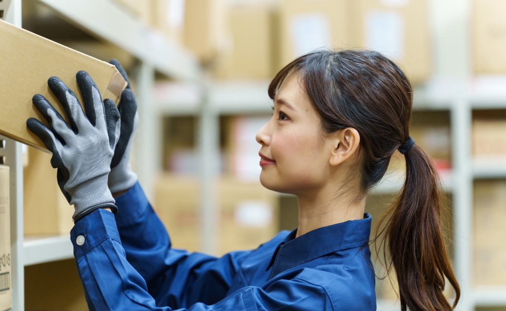 倉庫で箱を棚にしまう作業着の女性